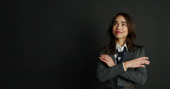 pretty girl business woman standing on a black background and smiling looking to the side and up. a girl in a jacket, a white shirt and a tie is smiling happily. promotion at work