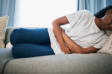 Period, stomach ache and black woman with pain on sofa holding belly from sickness, cramps and digestion. Menstruation, endometriosis and girl on couch with menstrual problem, pms and bloated abdomen - obrazy, fototapety, plakaty