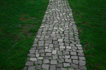 Stone block walk path. park background. pedestrian way made of gray granite paving stones in a park with green grass near a pedestrian paved path for walking in the garden, landscape, nobody.