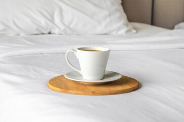cup of freshly brewed coffee stands on wooden tray on clean white made bed. Concept of good morning