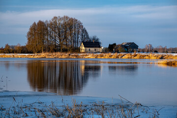 country house on river bank between trees in sunny winter evening, Lielupe river, Latvia.