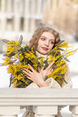 A young woman stands with a bouquet of yellow mimosa and sniffs the flowers. The concept of the Spring holiday - March 8, Easter, Women's Day