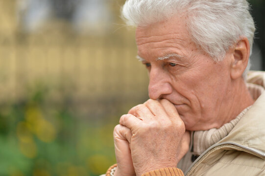 Serious old man thinking in park on green background