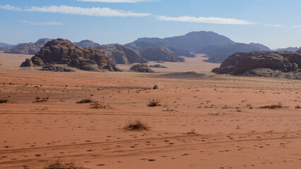 Fototapeta na wymiar Solo four wheel drive truck driving through vast, remote wilderness of Arabian Wadi Rum desert with red sandy terrain and rugged mountainous landscape in Jordan