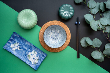 Japanese or Chinese table setting with traditional table mat and dinnerware with green and black background. Eating, dining, food and drink concept. Flat lay, top view and copy space.