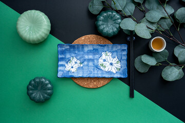 Japanese or Chinese table setting with traditional table mat and dinnerware with green and black background. Eating, dining, food and drink concept. Flat lay, top view and copy space.