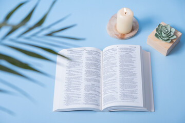 Fototapeta na wymiar Open Holy Bible with candles and palm leaves on blue background
