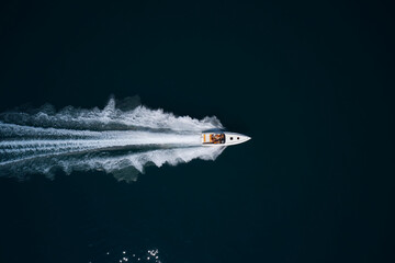 Big white high performance motorboat with orange seats move faster on dark water top view