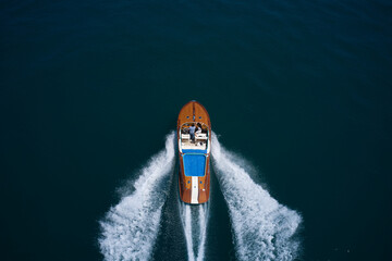 Luxurious wooden big boat with people moving fast on dark water top view. Couple man and woman luxury boat on the water top view. - obrazy, fototapety, plakaty