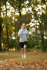 a caucasian girl in a blue sweatshirt puts on headphones in the park and prepares to run. pretty young woman puts on headphones. Pretty smiling woman puts on headphones in the park before jogging.