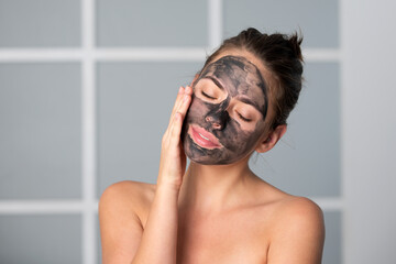 Woman apply charcoal facial mask mask isolated at home. Spa, cosmetic mask. Beautiful woman with black clay facial mask. Skin care, peeling, moisturising and beauty treatment.