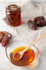 Natural organic healthy date syrup in a glass bowl with wood spoon and whole dates on the background