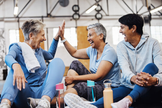 Gym, high five and group of mature women celebrate after fitness class, conversation and congratulations on floor. Exercise, bonding and happy senior woman with friends sitting together at workout.