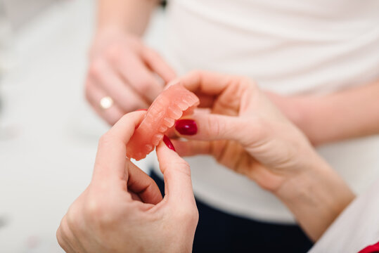 Acrylic denture prosthesis of upper jaws in hands woman. Sample for dental training. Removable plastic denture. Upper jaws with fake teeth. Dentures or false teeth. Sample for studying dentistry.