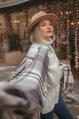 A girl in a plaid stole walks around the city and smiles, in a white sweater