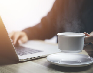 Man working in front of a laptop with hot coffee with smoke and steam	
