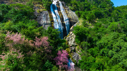 Wide aerial view of waterfall flowing in the depths of the forest. Beautifu large waterfall in the forest. Natural landscape, deep green forest and plants surrounded. Water flow from stones.