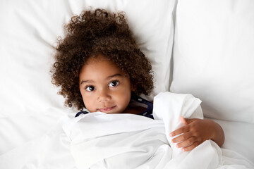 Young girl with afro hair lying on white bed