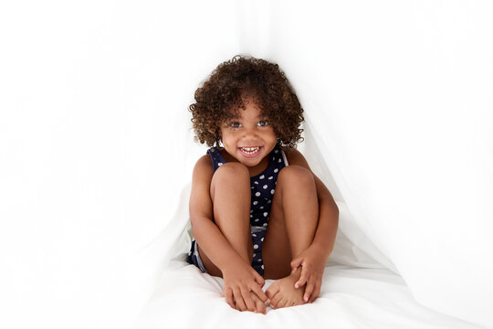 Happy little girl with afro hair hiding under white sheet