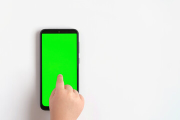 Child hand touching clicking on mobile phone with chromakey screen. Little Baby Finger Taps in the center of blank phone green display. Close up. Using smartphone device. Top view Flat lay
