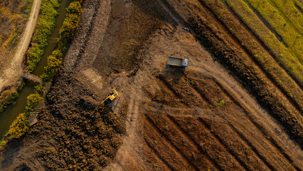 Aerial view of a wheel loader excavator with a backhoe loading sand onto a heavy earthmover at a construction site.