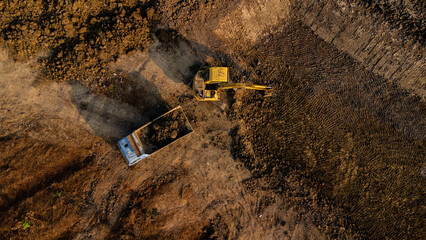Aerial view of a wheel loader excavator with a backhoe loading sand onto a heavy earthmover at a...
