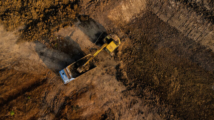 Aerial view of a wheel loader excavator with a backhoe loading sand into a heavy earthmover at a construction site. Excavator digging soil pits for the agricultural industry.