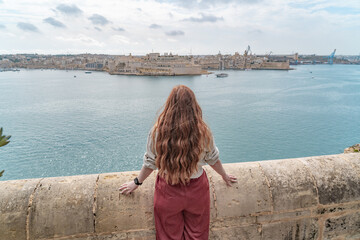 Fototapeta na wymiar woman standin at a wall looking at a panoramic view of the three cities in valletta