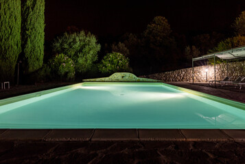 Illuminated swimming pool on the Montemassi hillside surrounded by cypresses and oleanders n the province of Grosseto. Italy