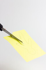 Steel scissors on a white background cut a silhouette of a person from yellow colored paper. Paper application. Metal scissors with black handles. Horizontal format. Handmade, craft, work with paper.