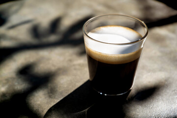Clear cup of americano macchiato coffee  with  shadow of tree branch on desk  in the morning