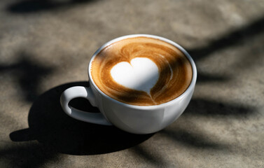 Cup of  heart shape  latte art coffee  with  shadow of tree branch on desk  in the morning