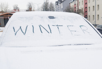 The word winter written on a snow-covered car window.