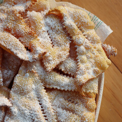 Italian Carnival pastry. Traditional carnival sweet crisp pastry deep-fried and sprinkled with powdered sugar. Chiacchere or crostoli, bugie, cenci  in a white plate on wooden table 