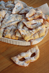 Italian Carnival pastry in shape of  a Mask. Traditional carnival sweet crisp pastry deep-fried and sprinkled with powdered sugar. Chiacchere or crostoli, bugie, cenci  in a white plate on wooden tabl