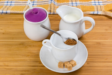 Instant coffee granules in spoon atop empty cup, milk, sugar