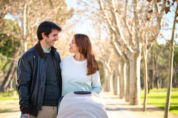 Couple looking at each other with a baby stroller in a park.