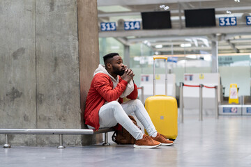 Sad African American man upset at airport his flight is delayed. Depressed traveler male waiting...