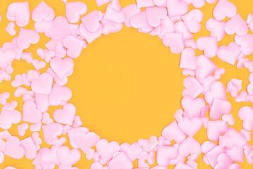 Round frame made of textile pink confetti in a heart shape on a yellow background. Copy space.