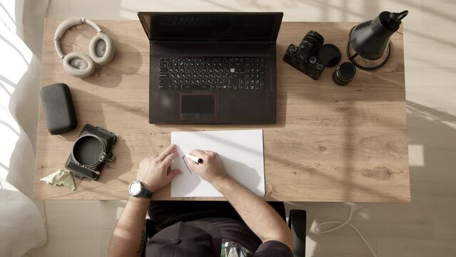 unrecognizable male freelancer in black cap sits at table and writes word PEACE on A4 paper. concept no war. peaceful inscription on paper. international sign of peace and love, hippies.