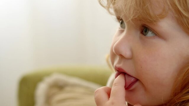 extreme close up view of child watching TV and sucking her thumb. Fascinating cartoons are shown on TV for smallest people on earth. Curly-haired child girl is watching cartoons or movie intently.