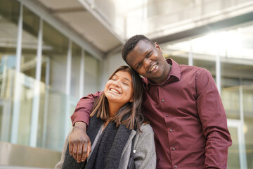 Obraz premium Young smiling multiethnic couple hugging outside the office. diverse executive couple