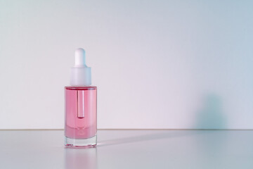 Pink face oil in glass bottle with white pipette dropper cap. Body care cosmetics background with copy space