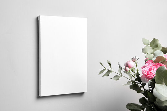 White canvas mockup hanging on grey wall and bouquet of pink roses with eucalyptus leaves. Blank canvas, interior decor