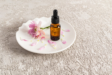 a cosmetic bottle with an amber glass dropper stands on a ceramic white plate with a lilac flower and petals. natural cosmetic product for care.