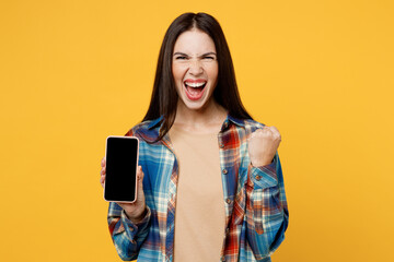 Young excited happy cool woman wear blue shirt beige t-shirt hold in hand use mobile cell phone with blank screen workspace area do winner gesture isolated on plain yellow background studio portrait.