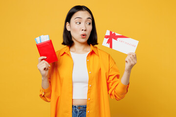 Young amazed woman in casual clothes hold passport ticket gift voucher card isolated on plain yellow background. Tourist travel abroad in free spare time rest getaway Air flight trip journey concept