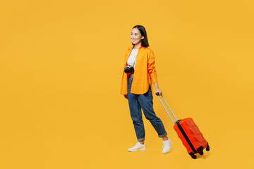 Side view young woman wear summer casual clothes walking go with suitcase isolated on plain yellow background. Tourist travel abroad in free spare time rest getaway. Air flight trip journey concept.