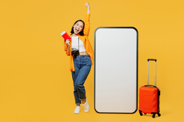 Young woman wear summer clothes big blank screen mobile cell phone hold passport ticket isolated on plain yellow background. Tourist travel abroad in spare time rest getaway. Air flight trip concept.