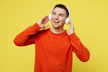 Young minded fun caucasian man wear orange casual clothes headphones listen to music looking aside in reverie mood isolated on plain yellow color background studio portrait. People lifestyle concept.